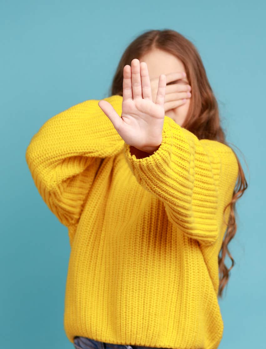 Covering her eyes, she uses the other hand to express a healthy boundary