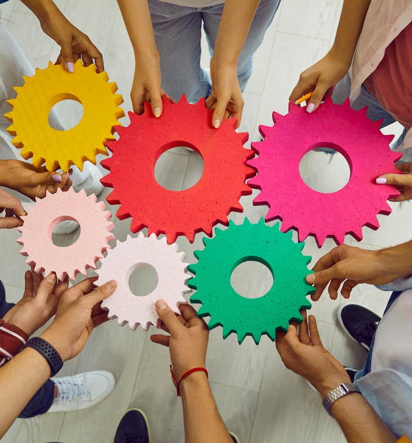 Group of people hold enmeshed gears symbolic of progress over perfection