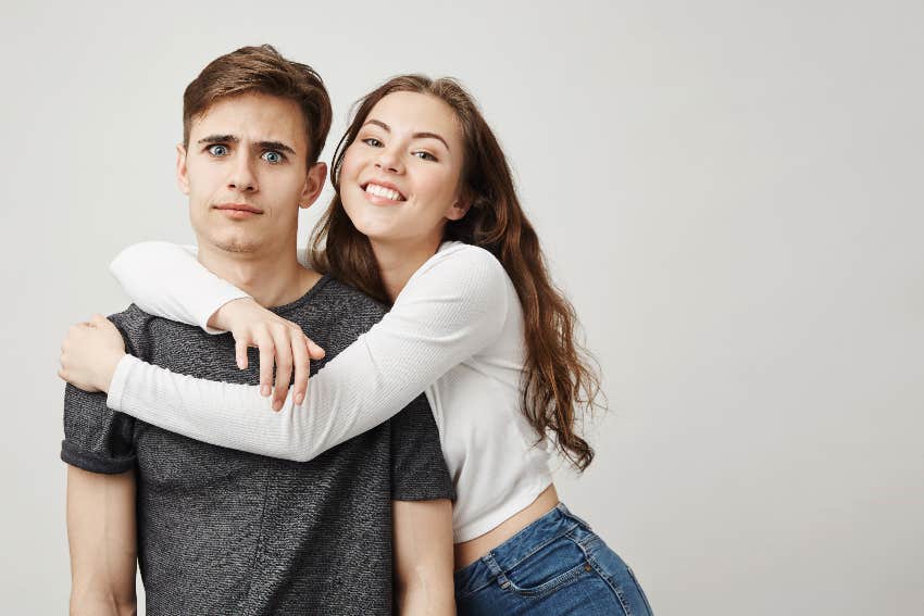 woman clinging onto man while he looks uncomfortable 