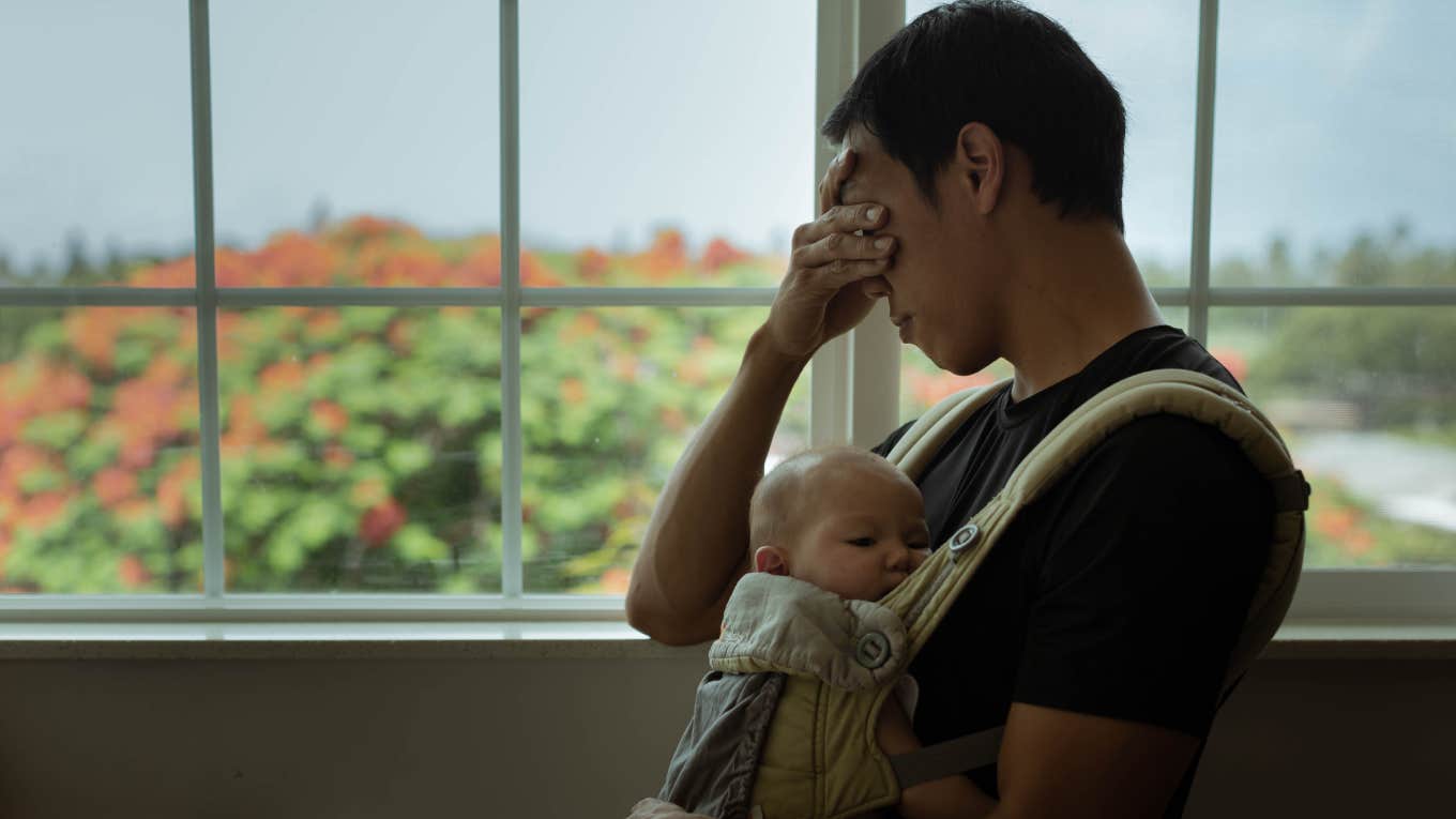 stressed out father holding his sleeping baby at home.