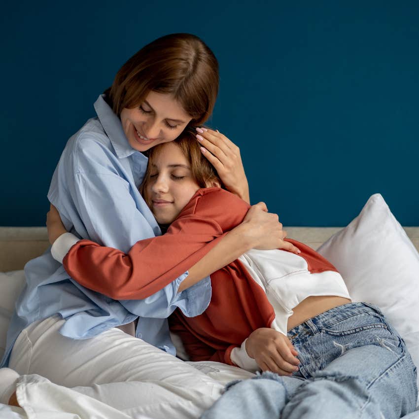 Teenage daughter and mom hugging in bed after working night shift. 