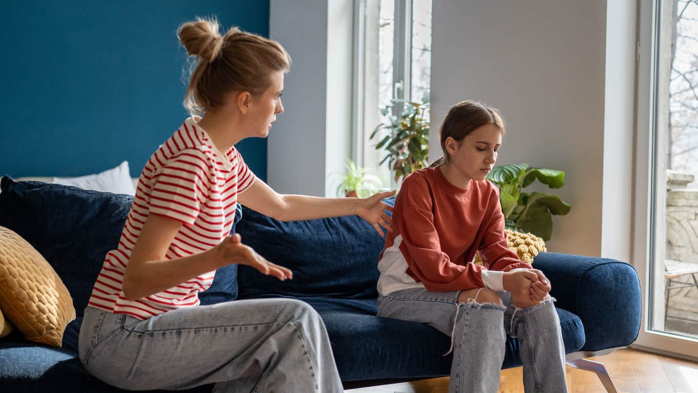  mother trying to speak with upset teen daughter while sitting together on sofa at home