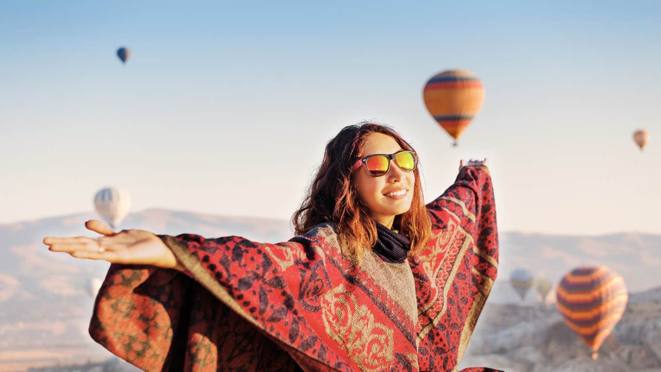 Woman standing on top of mountain with air balloons, top two percent 