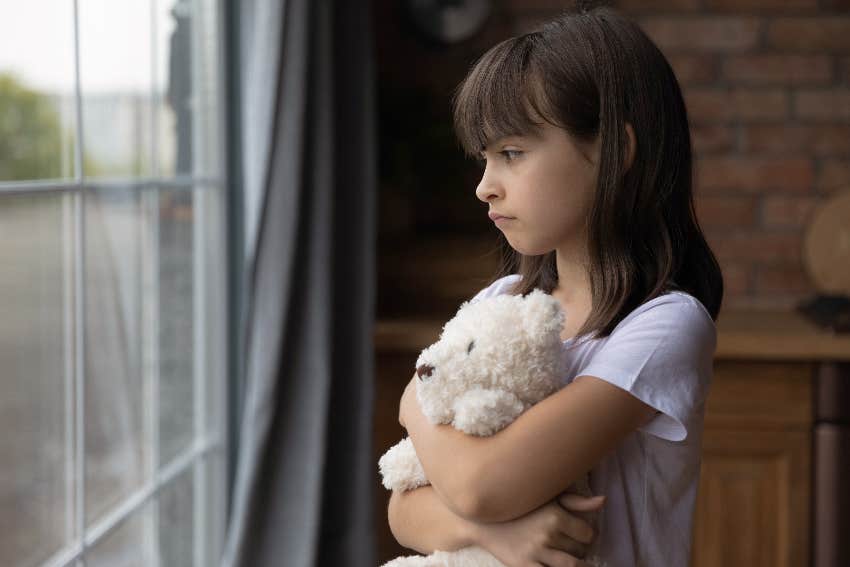 little girl holding stuffed animal while looking out window