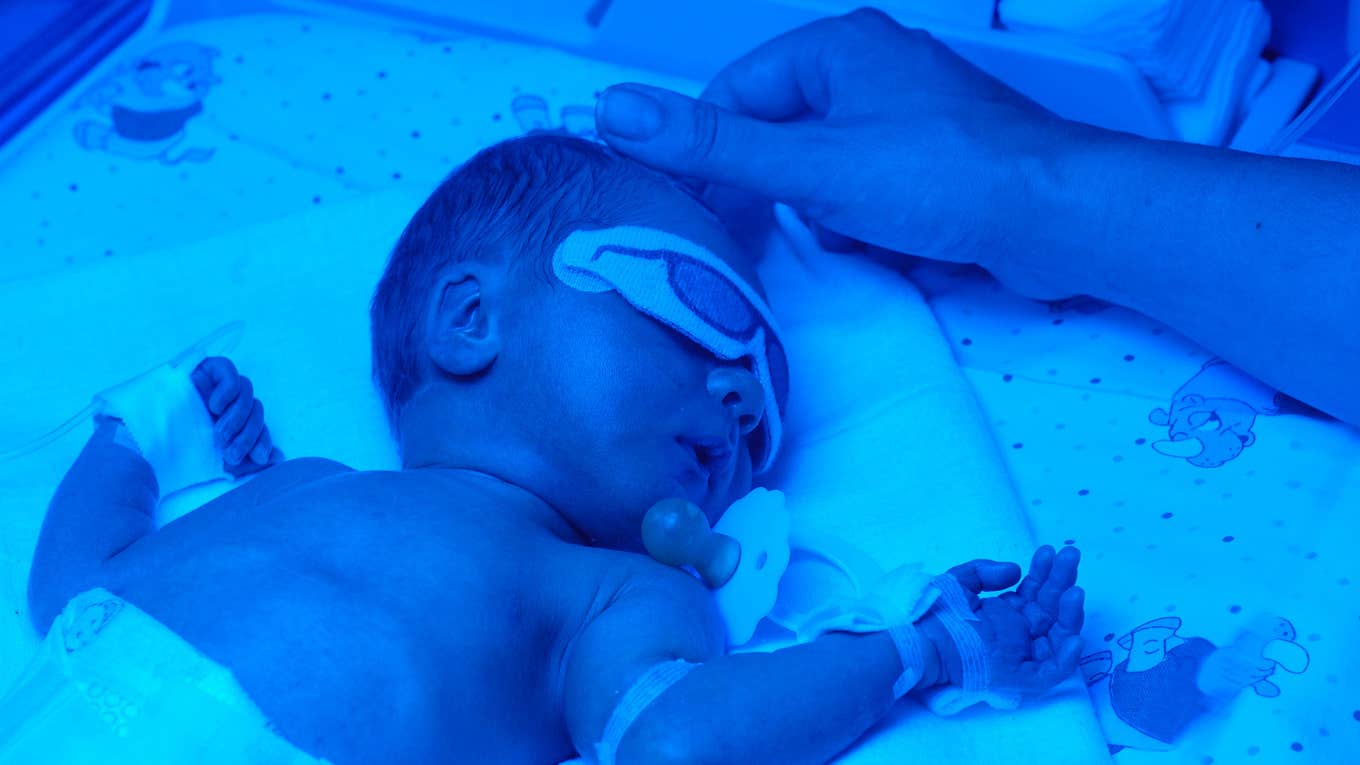 Baby in blue light bed, mothers hand touching his head