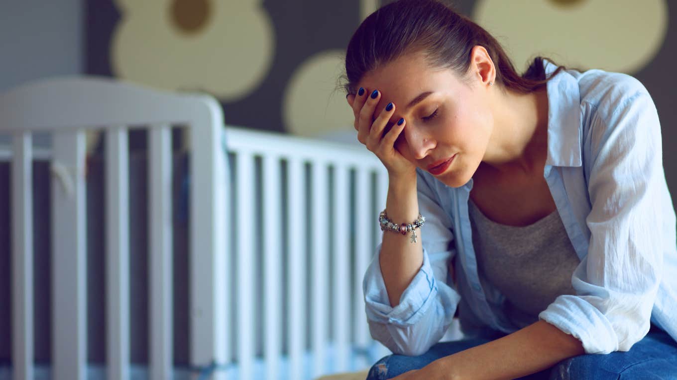 frustrated woman sitting near crib