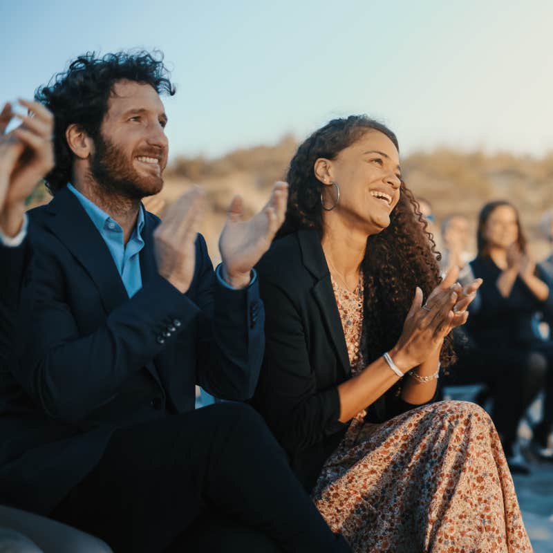 Excited guests sit in an outdoor venue and clap their hands