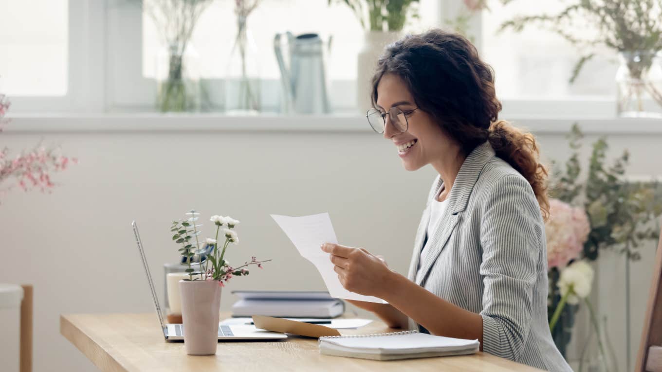 woman smiling while reading paper and sitting at desk