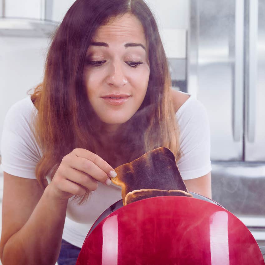 Woman taking burned toast out of red toaster
