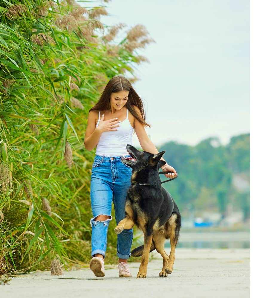 Woman in white tank top walking her German Shepherd