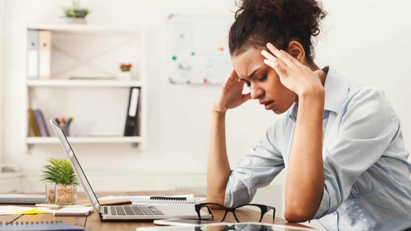 tired woman with fingers on temple sitting at desk in front of computer