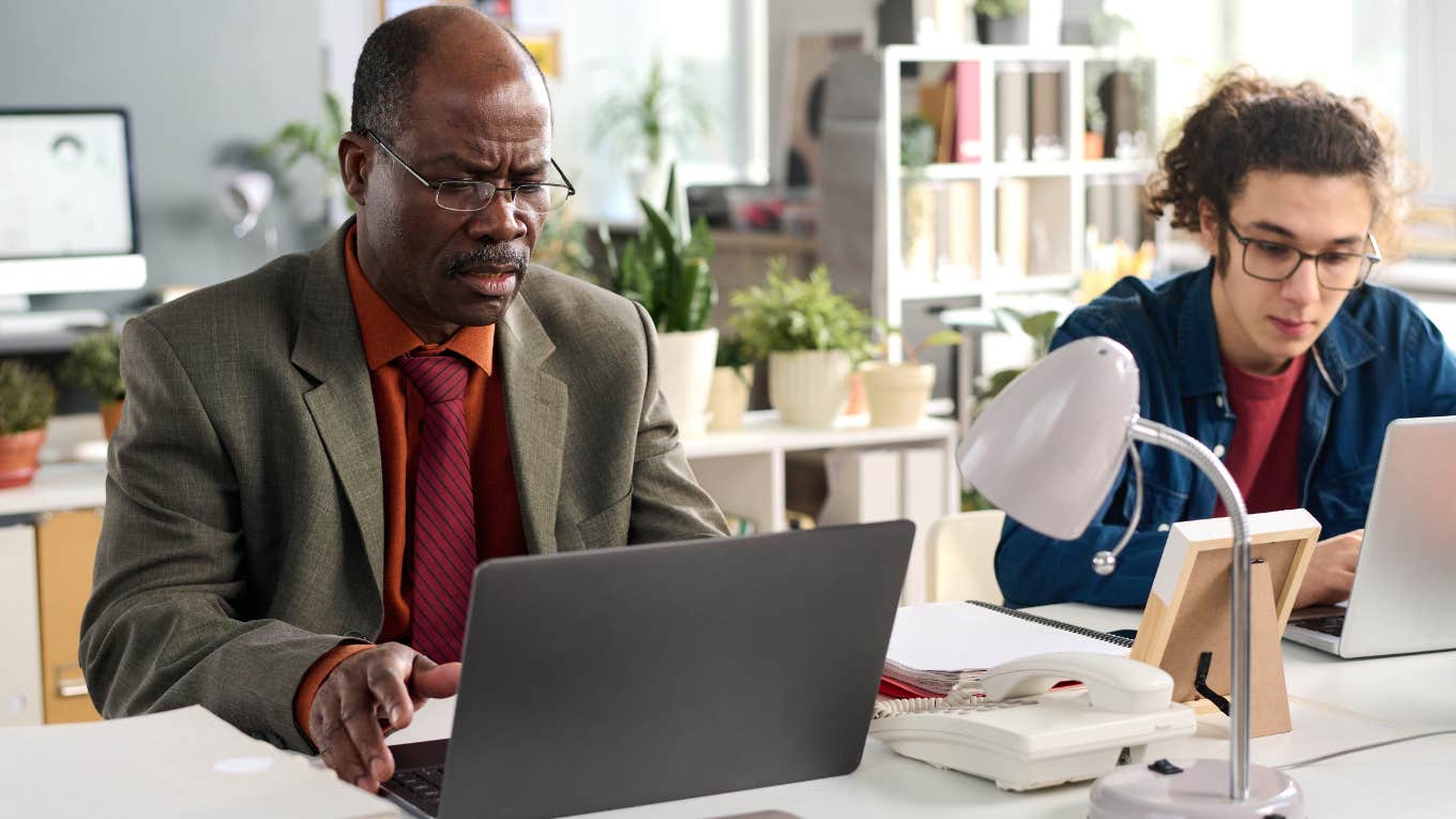 Boomer boss sitting with colleague doing Excel shortcuts.