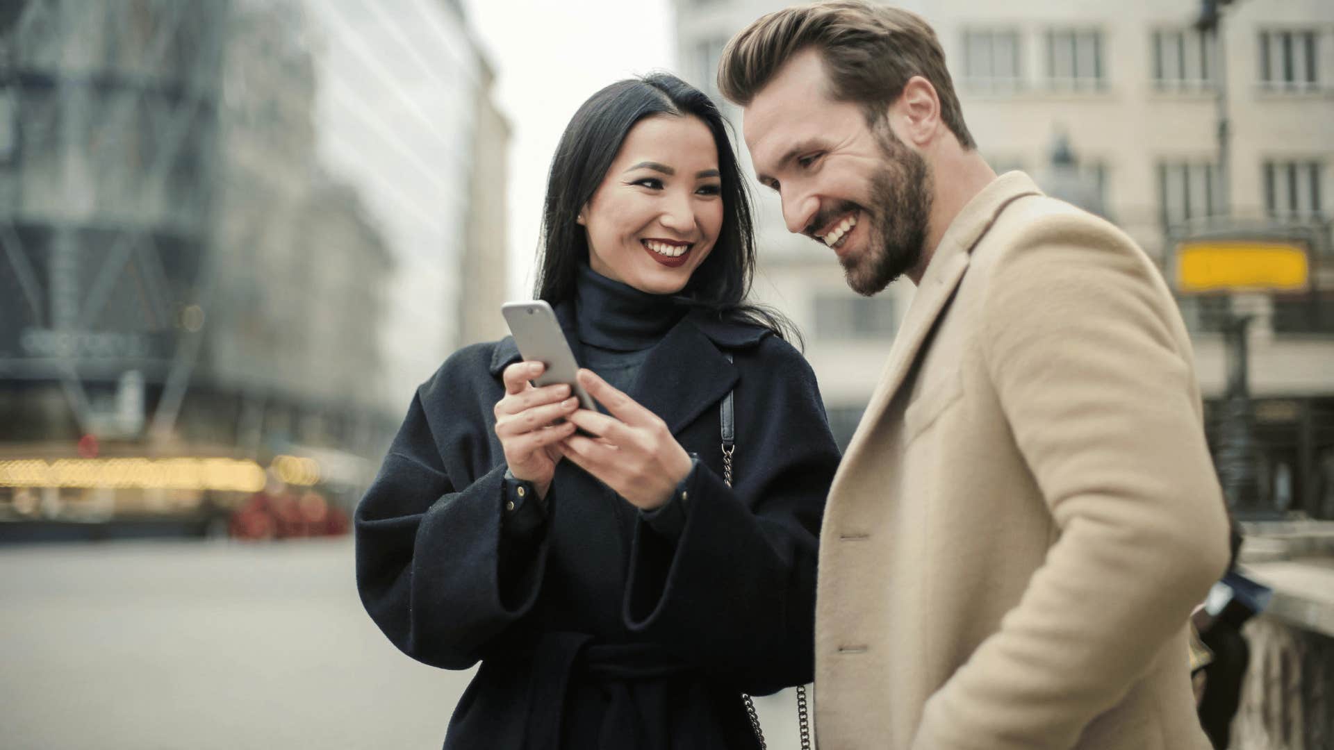 smiling woman showing phone to smiling man