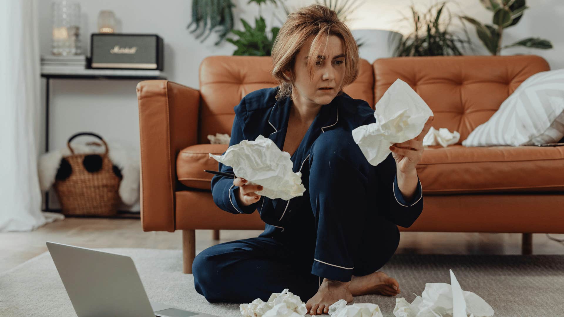 woman sitting on floor with laptop and crumpled paper