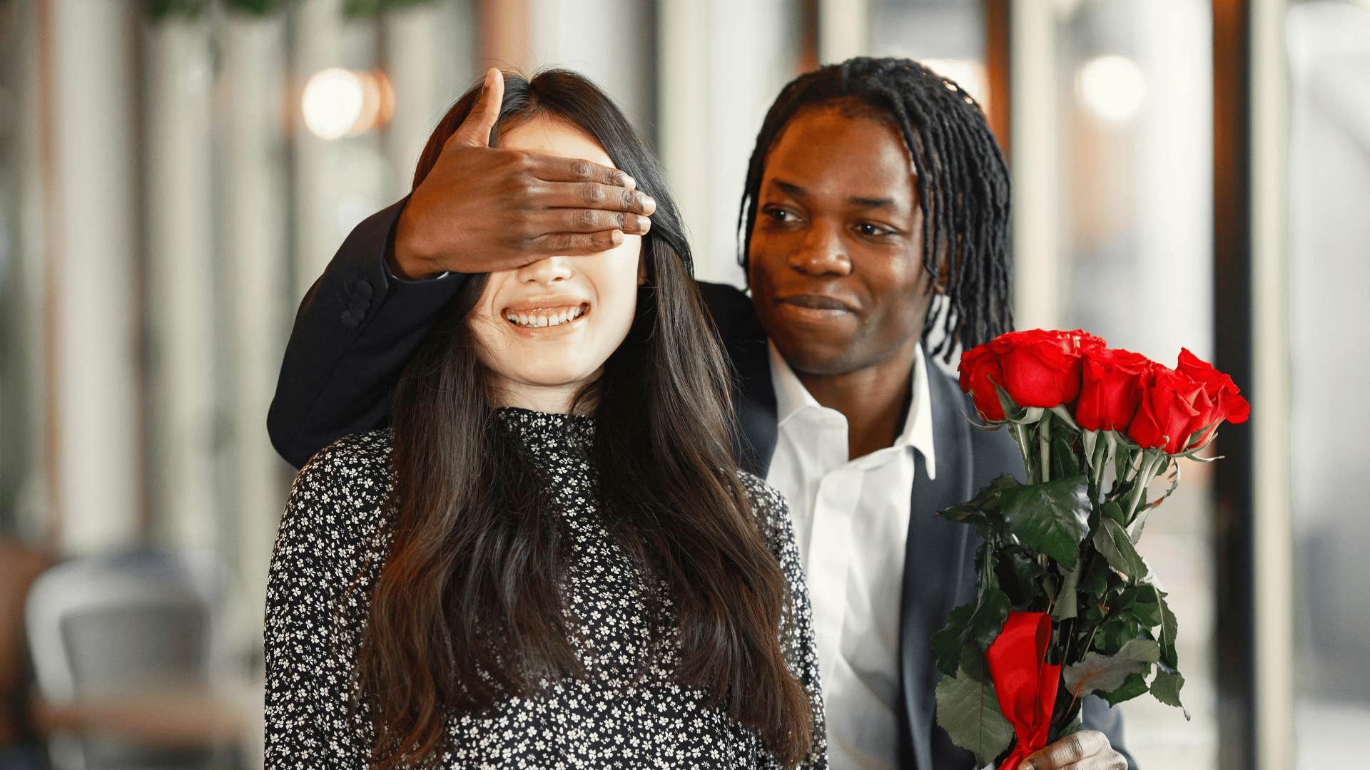 man with flowers behind woman and covering her eyes