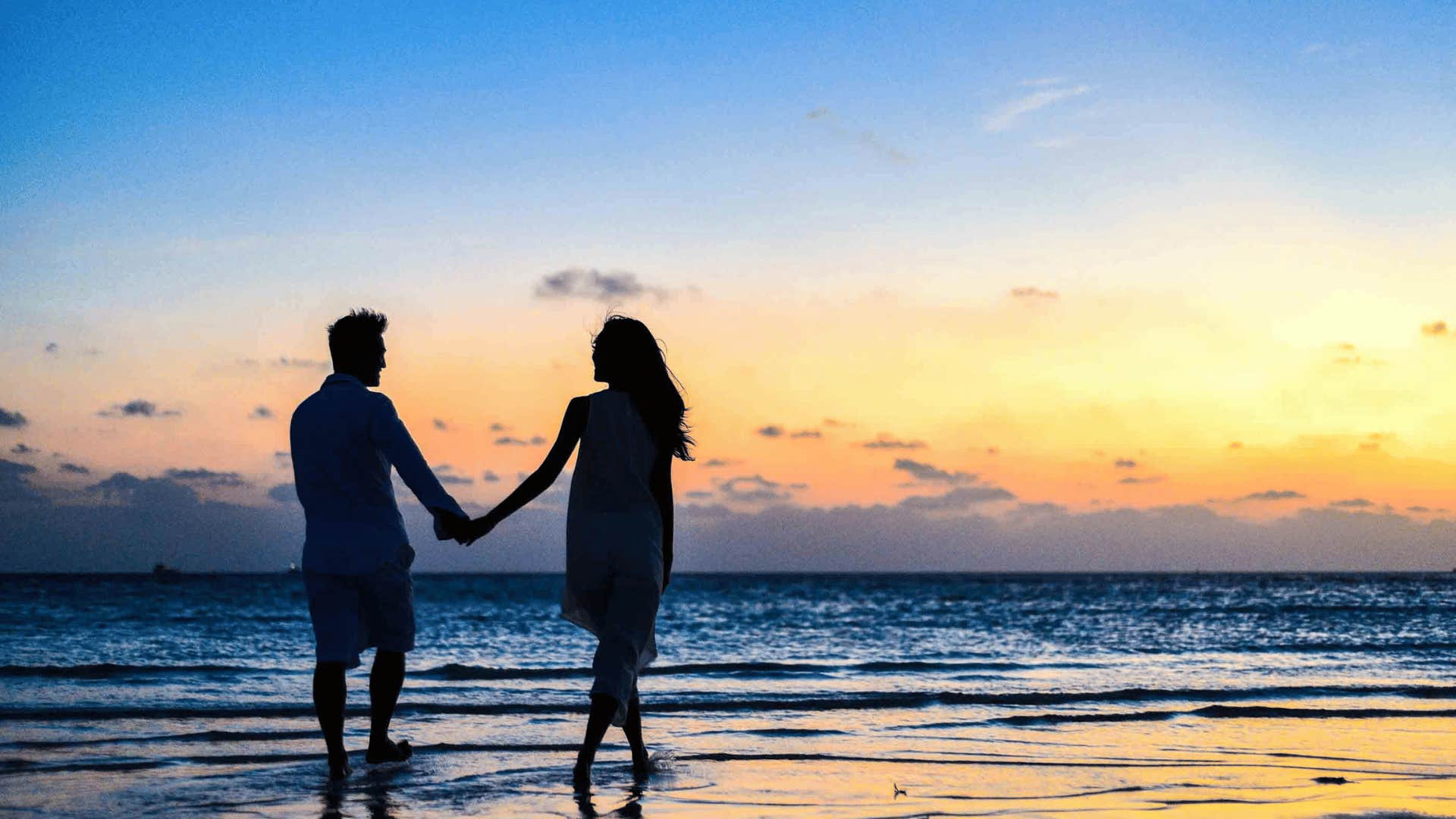 couple walking down beach at sunset