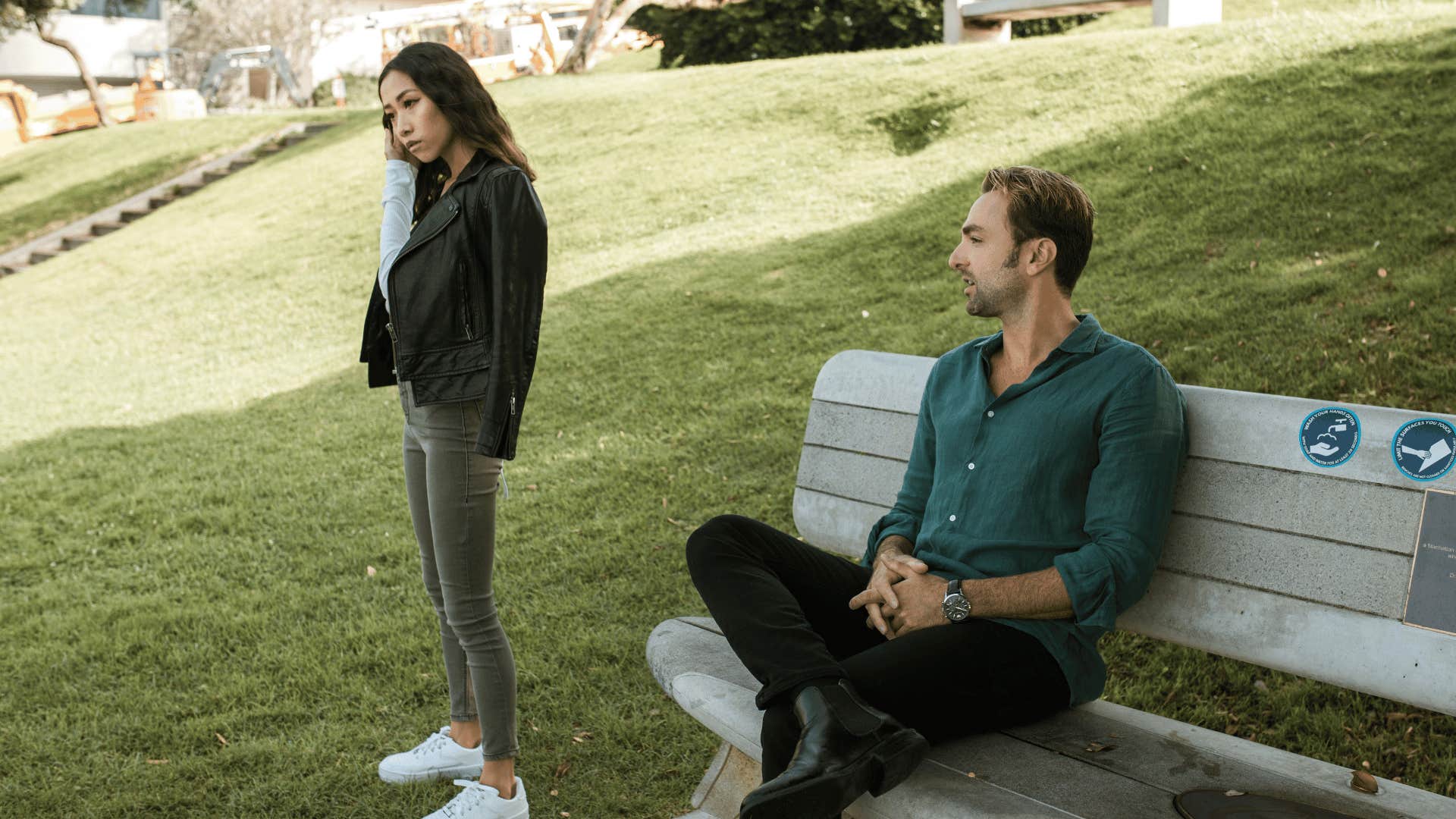 serious woman standing next to man sitting on bench