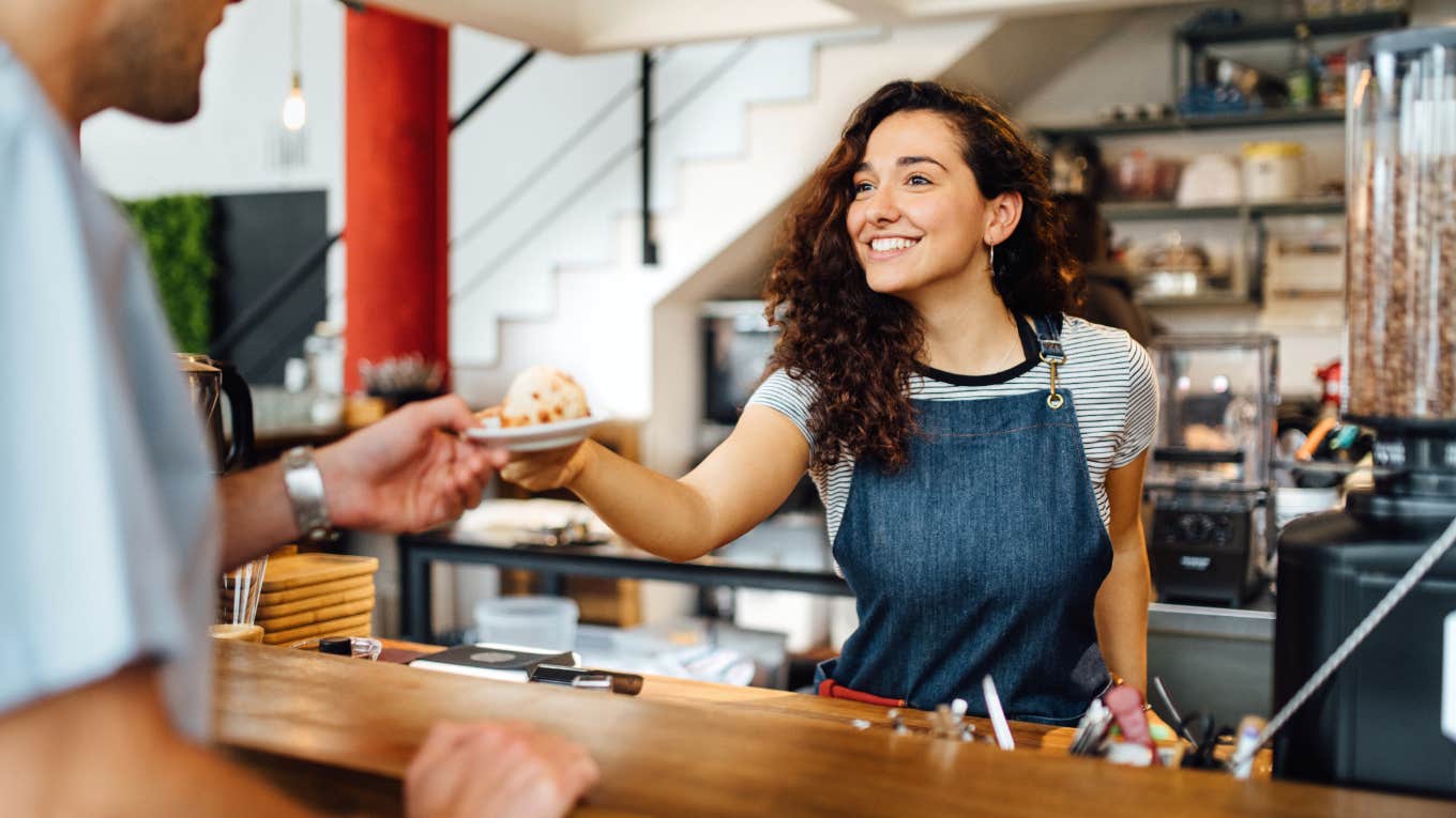 smiling kind barista handing customer pastry in coffee shop