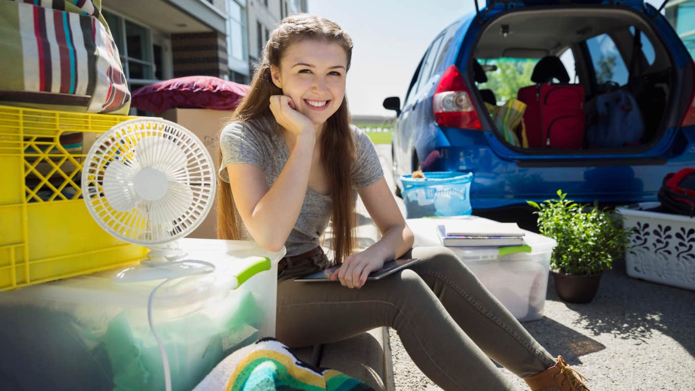 young college student sitting outside moving into college dorm on campus