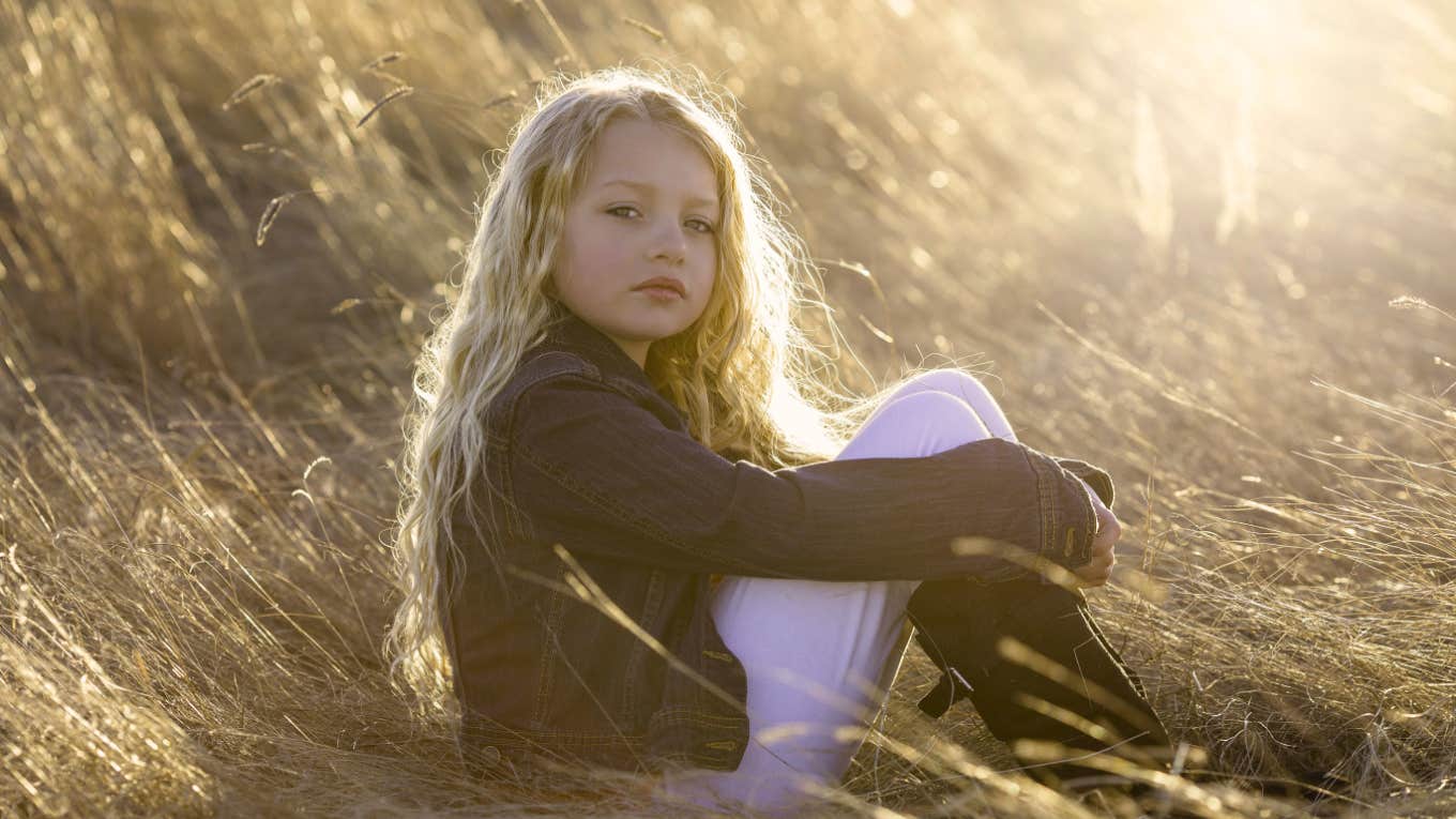 serious young blonde girl sitting outside in field