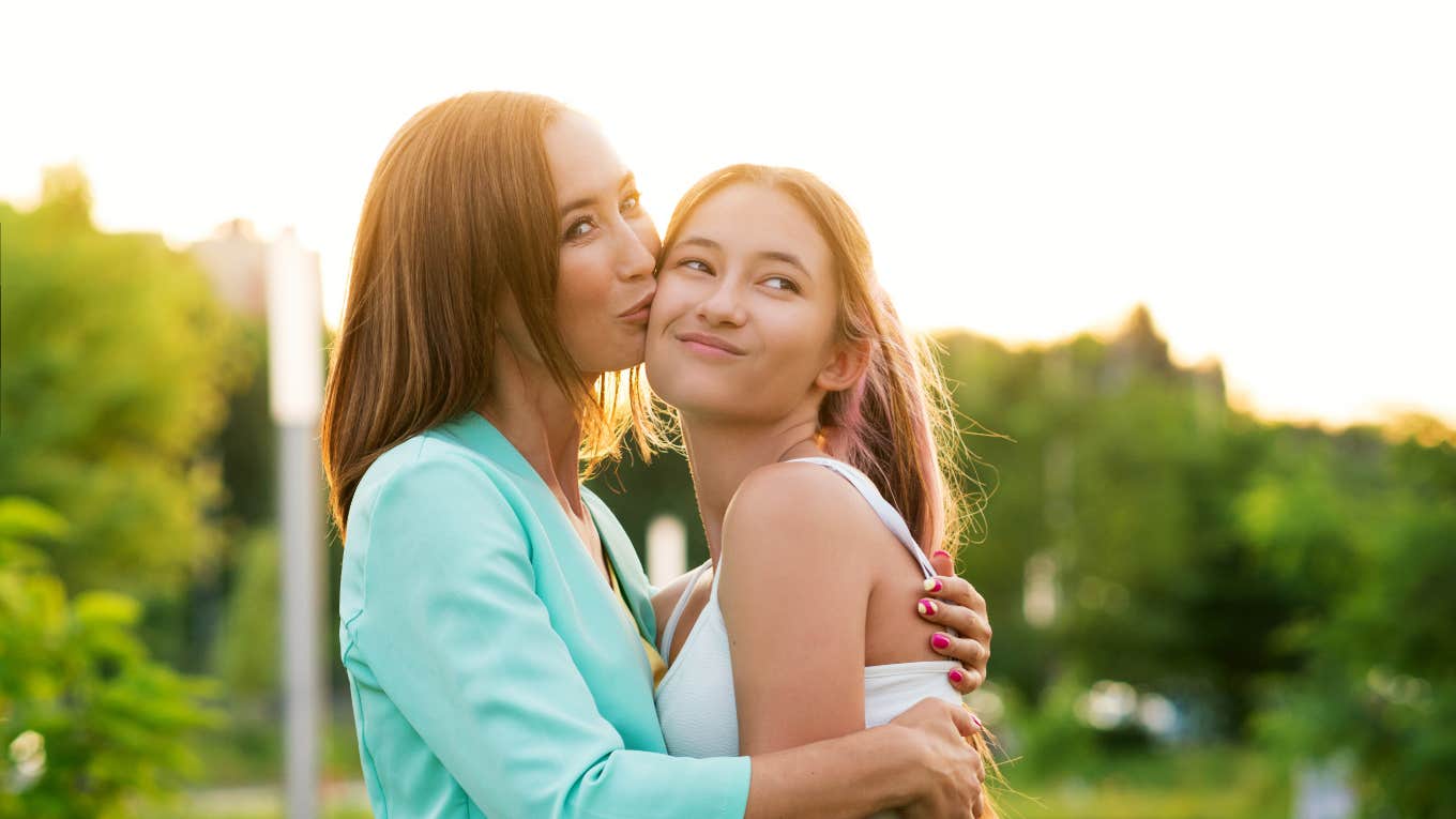 mom embracing and kissing her teen daughter's cheek outside