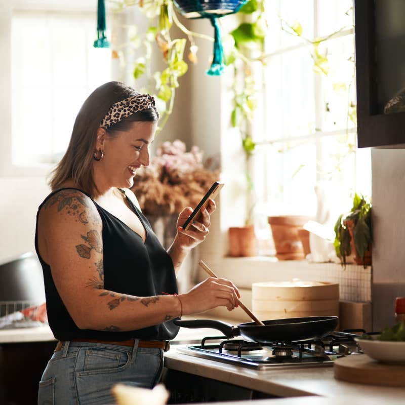 woman looking at phone while cooking in kitchen at stove