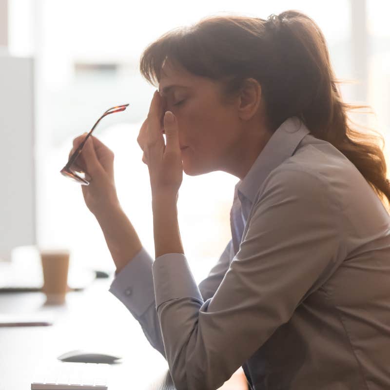 exhausted worker sitting at desk taking off glasses