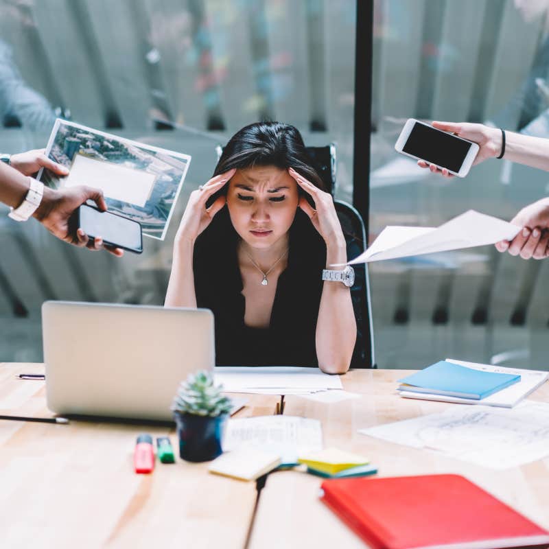 disappointed woman feeling headache from deadline surrounded by colleagues at workplace