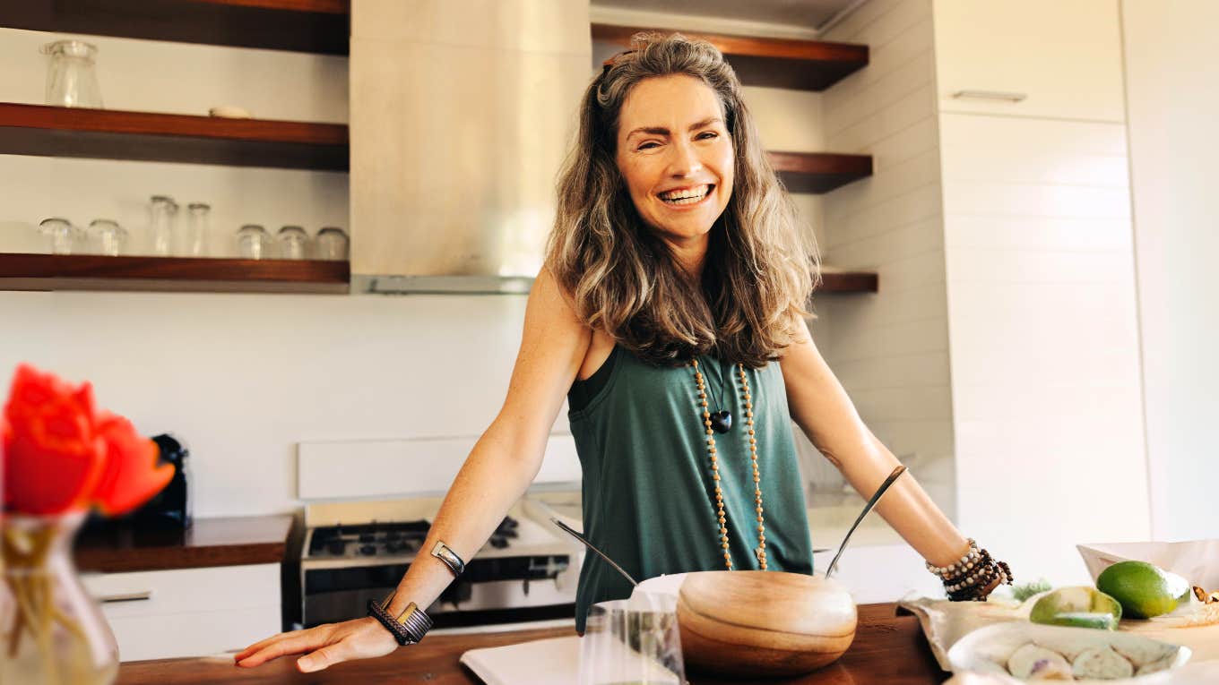 Woman attracting good vibes in decluttered kitchen, eating a healthy snack and watering her red flowers. 