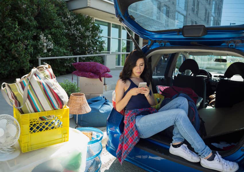 college student moving into dorm on campus sitting in trunk of car texting