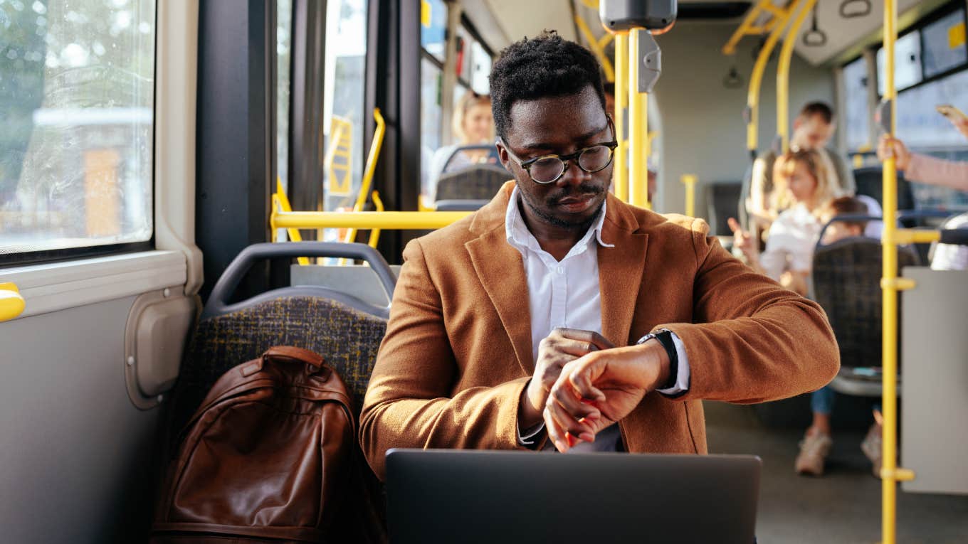 businessman in elegant suit traveling by bus to work and checking time on his watch