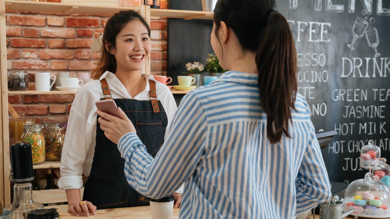 customer showing online payment on smartphone to waitress in cafe