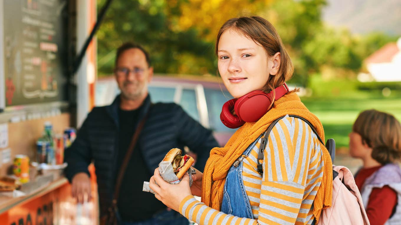 Teen daughter holding hamburger outside fast food restaurant