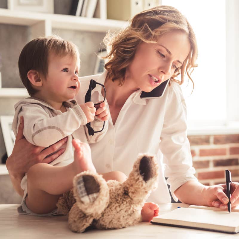 mom talking on phone and writing in notebook while holding baby