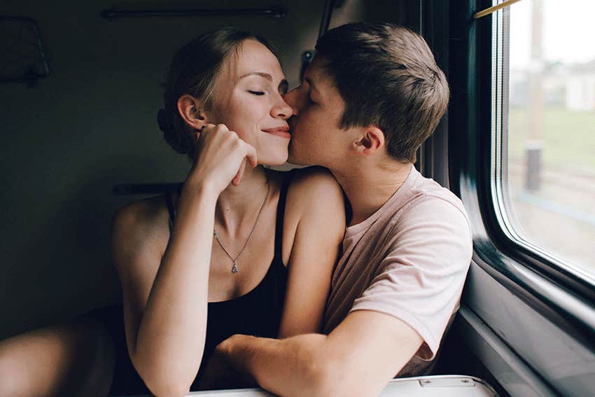 young couple hugging, kissing, telling secret near window.