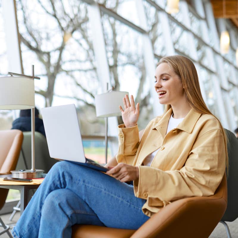 young woman smiling and waving while talking on laptop