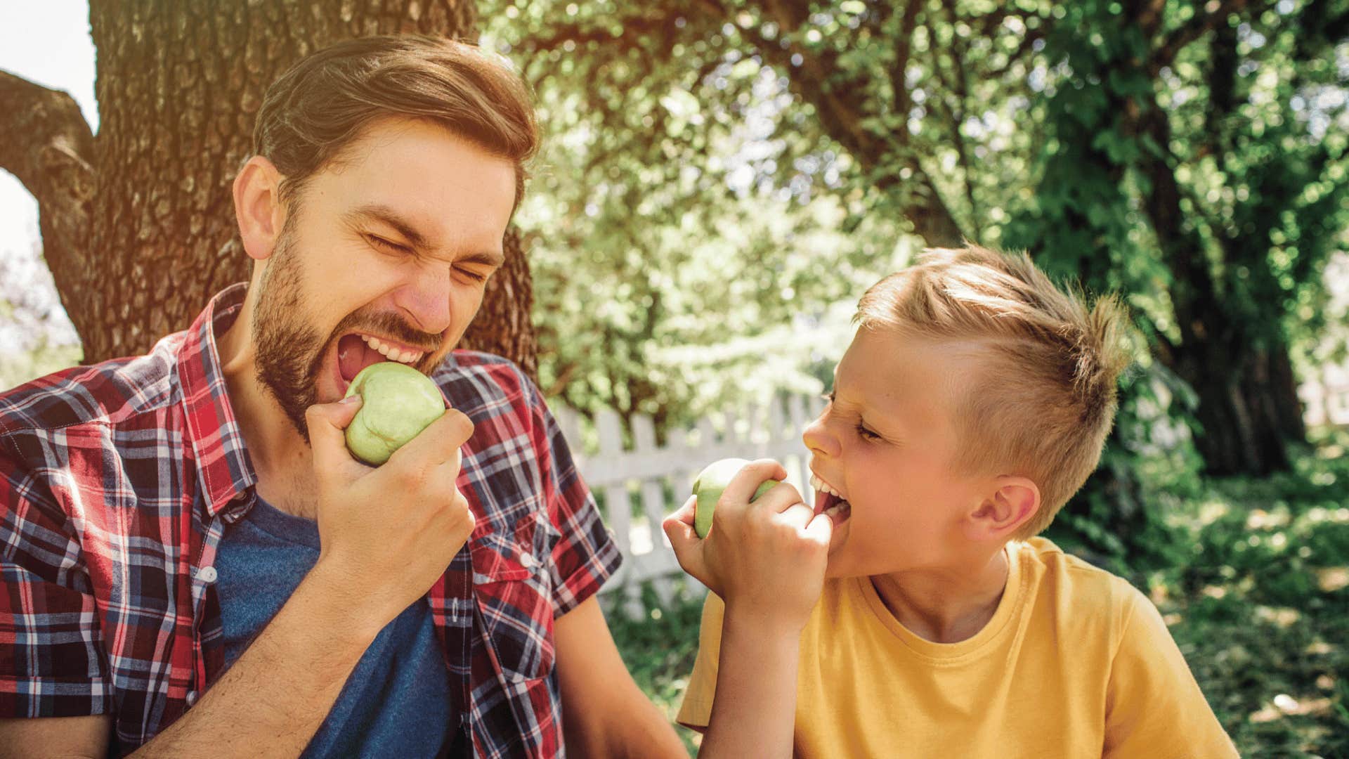 Man and son eating apples, enjoying nature 