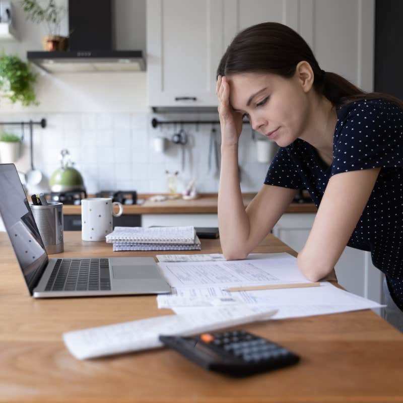 woman stressed about money sitting at laptop screen with papers and calculator