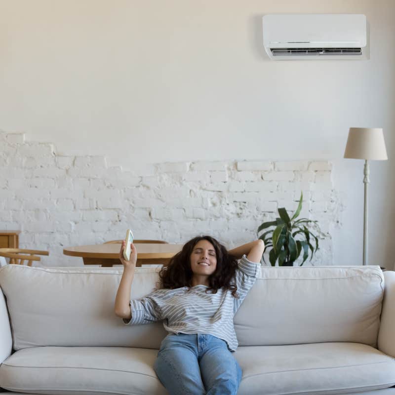 elaxed homeowner woman holding AC remote control sitting on couch in living room