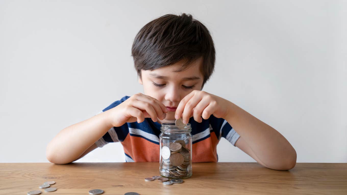 little boy sitting at table putting coins in a glass jar