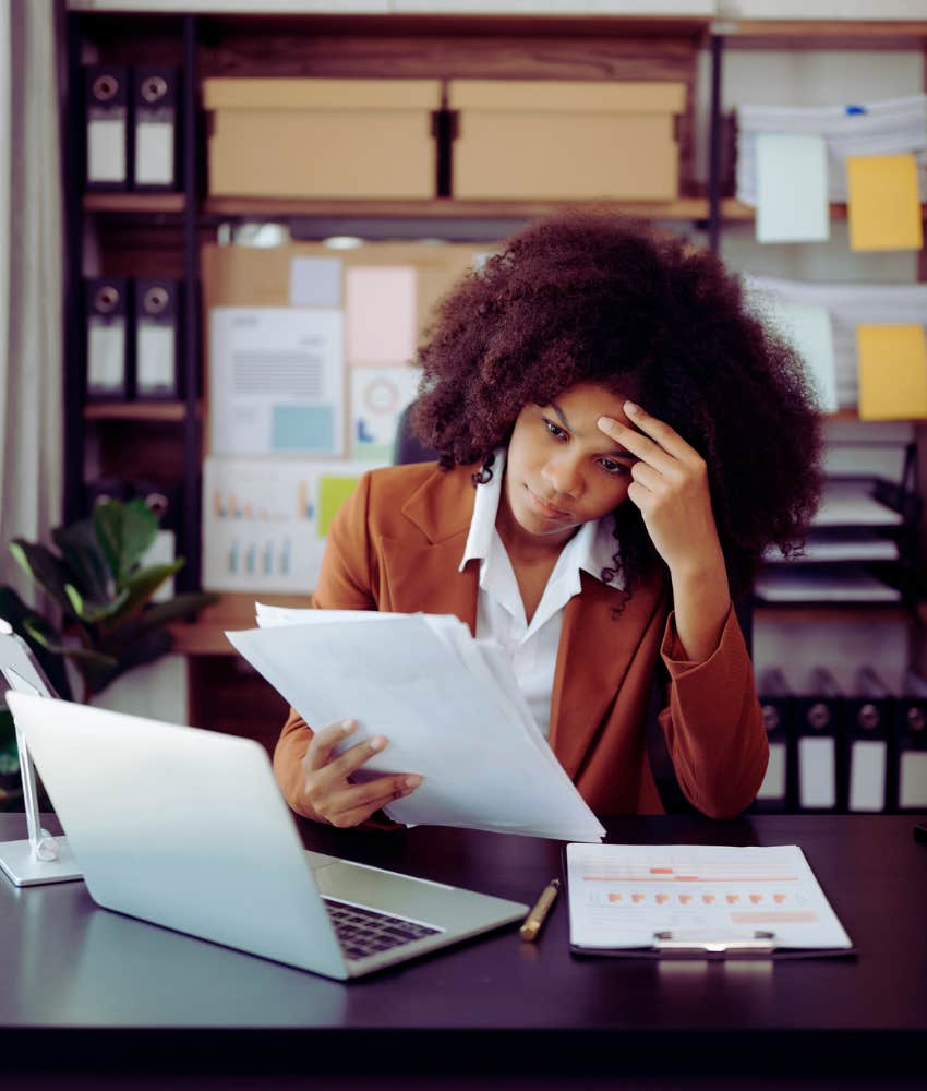 Female worker sitting at desk with hand on her head feeling overworked