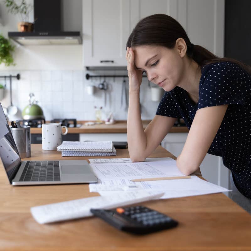 young woman thinking over domestic paperwork sitting in front of laptop