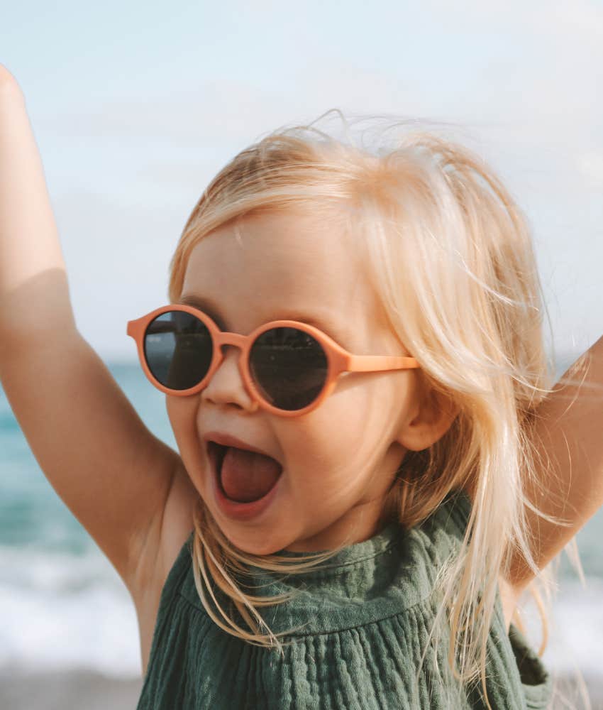 little girl with arms up wearing sunglasses and laughing