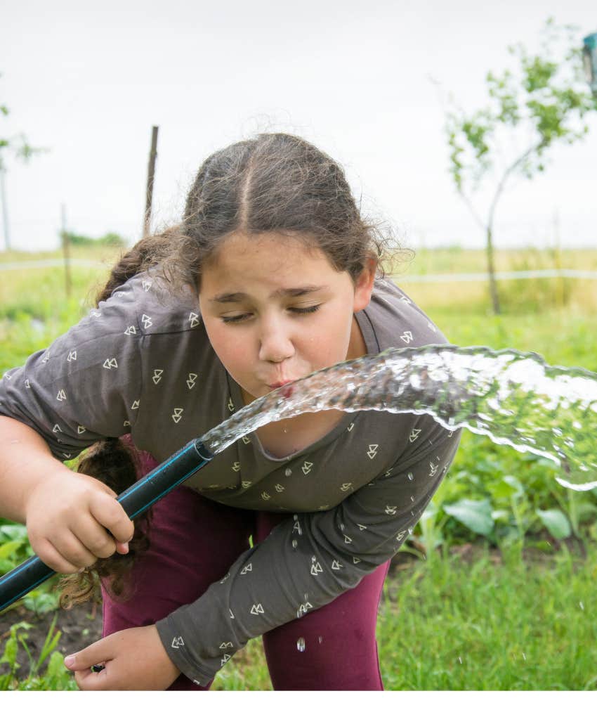 little girl drinking out of garden hose