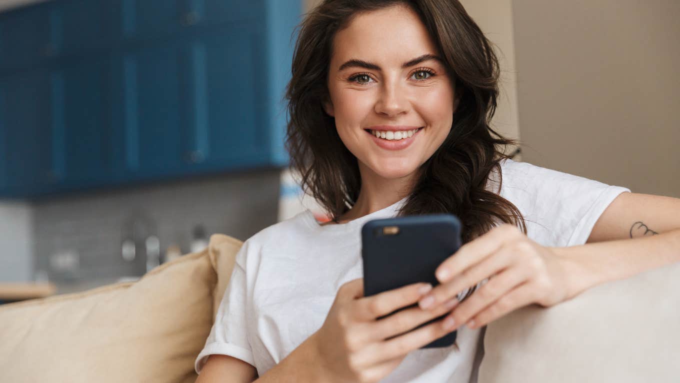 young woman smiling at camera holding her phone