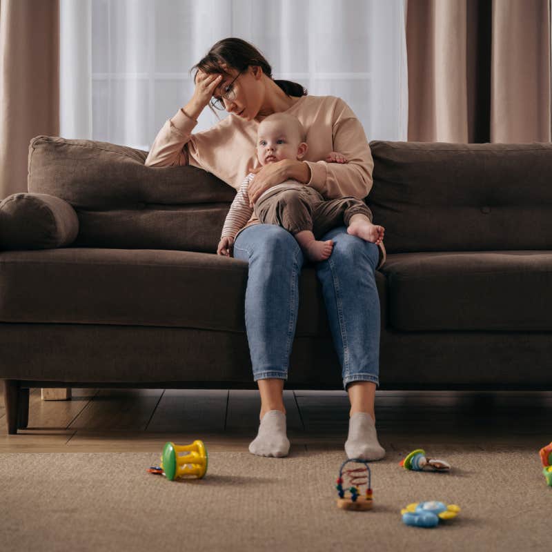 exhausted mom sitting on couch holding baby