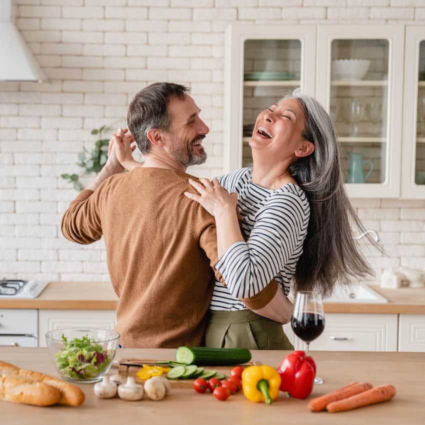 Happily married couple laughing while dancing and cooking