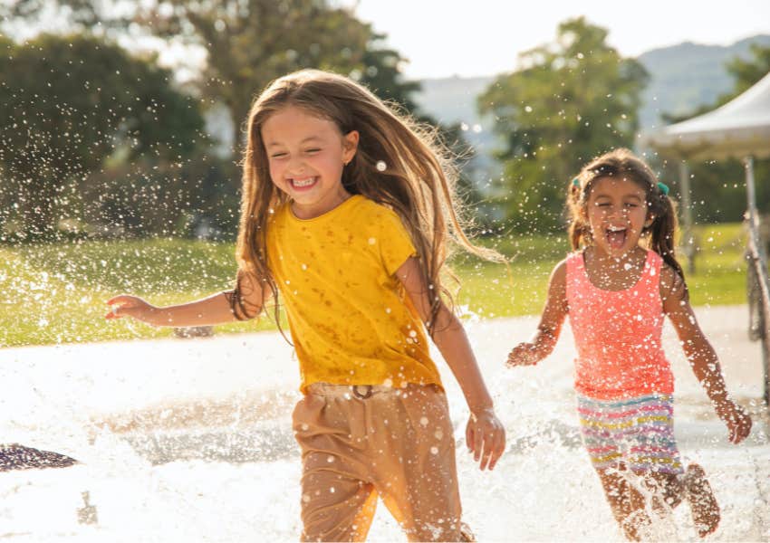 two happy girls laughing and running outside in sprinklers