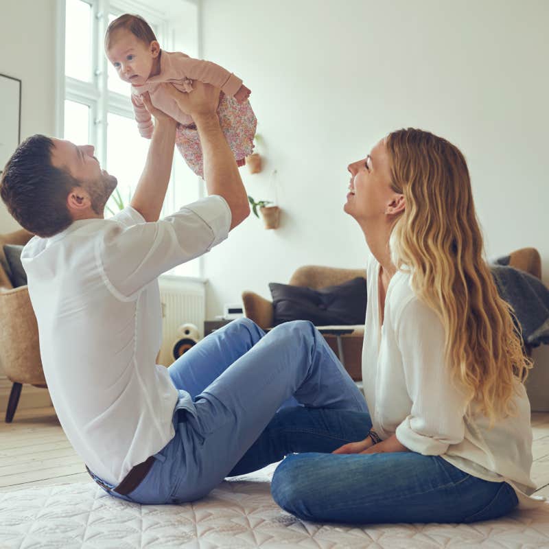  father holding his newborn baby daughter in the air with smiling mother sitting on the floor at home