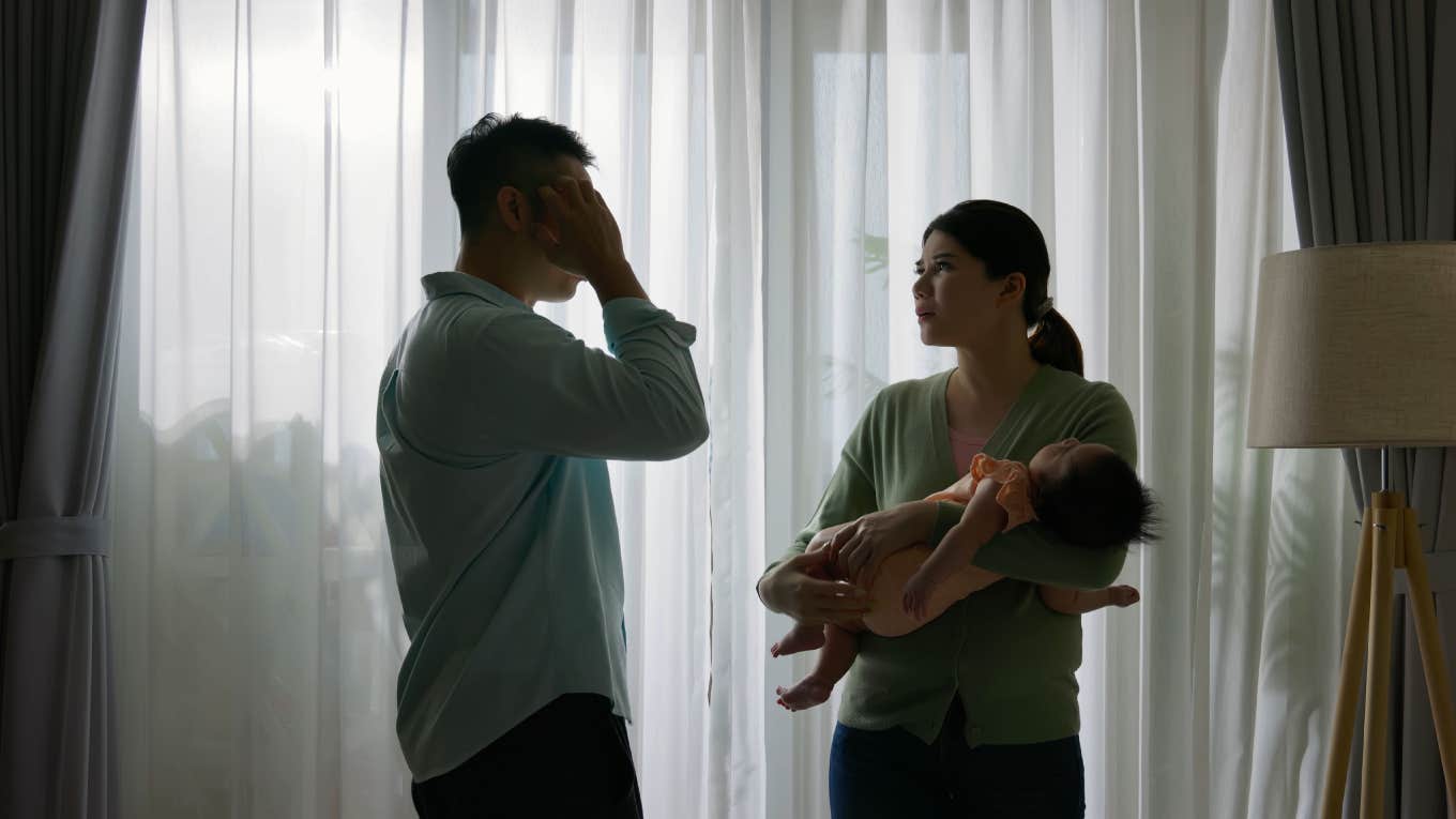 silhouette of young couple standing by windows with sleeping child are having conflict